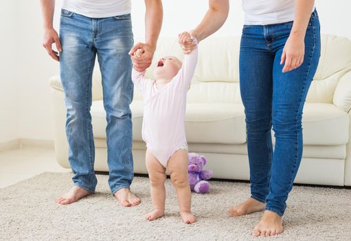 Family, children and parenthood concept - Parents teaching baby girl to walk.