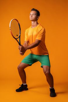 Full-length portrait of a tennis player man in action against orange background close up