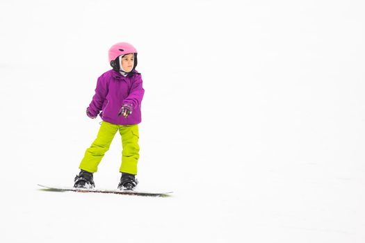 Snowboard Winter Sport. little girl learning to snowboard, wearing warm winter clothes. Winter background.