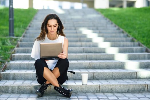 Middle-age businesswoman working with her laptop computer sitting on urban steps outdoors.