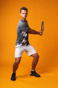 Full-length portrait of a tennis player man in action against orange background close up