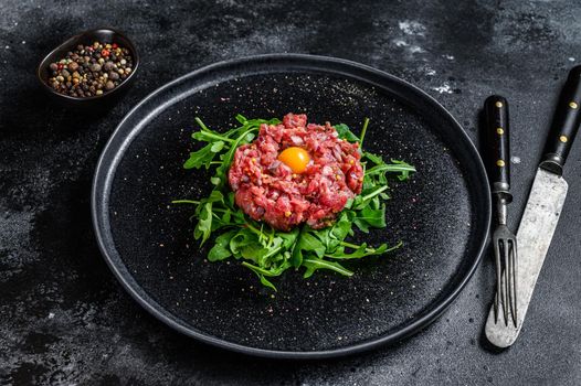 Beef tartar with a quail egg served on a black stone plate.. Black background. Top view.