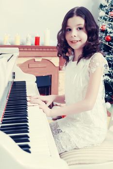 Adorable little girl new year's eve on the backdrop of the Christmas tree plays the piano.Creative toning of a photograph.