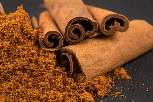 cinnamon sticks with powder on dark stone plate