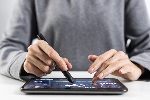 Woman using tablet computer for project management. Close-up of female hand holding pen and touching screen of tablet device. Online stock trading and investing. Mobile smart device in business