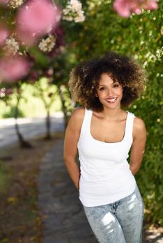 Young black woman with afro hairstyle smiling in urban park. Mixed girl wearing white t-shirt and blue jeans.