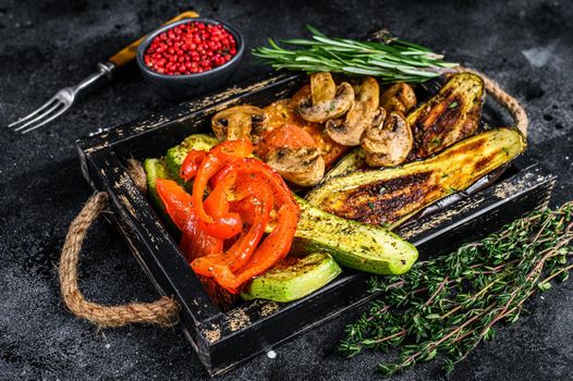 Baked vegetables bell pepper, zucchini, eggplant and tomato in a wooden tray. Black wooden background. Top view.