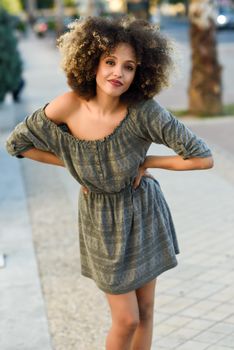 Young mixed woman with afro hairstyle smiling in urban background. Black girl wearing casual clothes.