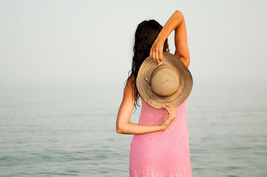 Portrait of a beautiful woman with long pink dress and sun hat on a tropical beach