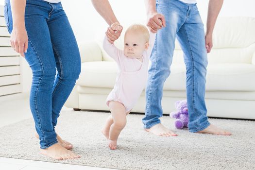 Family, children and parenthood concept - Parents teaching baby girl to walk.