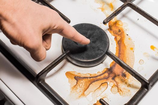 The guy's hand points a finger at the dirty plaque on the gas stove, close-up.