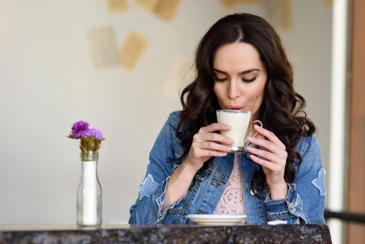 Young woman sitting indoor drinking coffee. Cool young modern caucasian female in her 20s. Cafe city lifestyle.