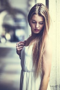 Portrait of beautiful blonde girl in urban background wearing white dress in urban background