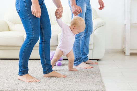 Family, children and parenthood concept - Parents teaching baby girl to walk.