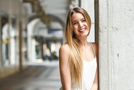 Portrait of beautiful blonde girl in urban background wearing white dress