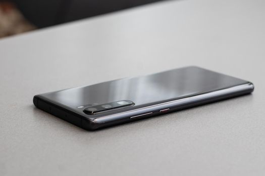 Black modern mobile phone with blank screen on black stone table background. Smartphone on old dark grey vintage texture background.