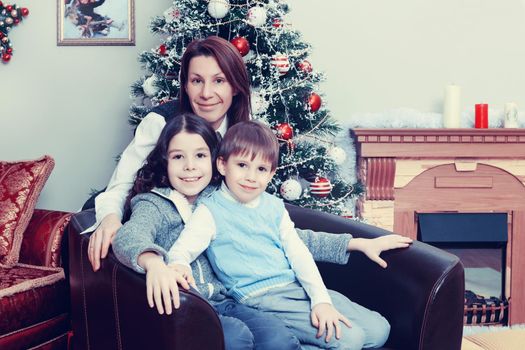 Happy mother hug her beloved children, daughter and son. On the couch by the Christmas tree.Creative toning of a photograph.
