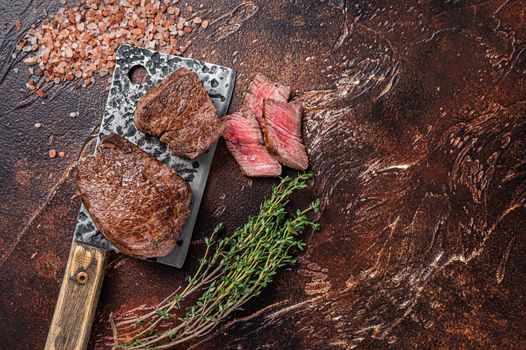 Rare Grilled fillet mignon beef steak on a meat cleaver. Dark background. Top view. Copy space.