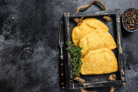 Raw chicken cordon bleu meat cutlets in a wooden tray with herbs. Black background. Top view. Copy space.