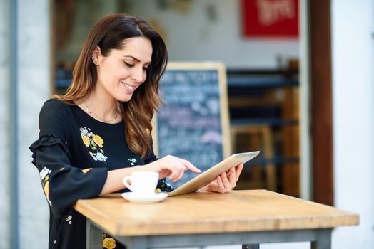 Young woman using tablet on coffee break in an urban cafe bar. Middle-aged female sitting at table at cafe. Girl with california highlights hairstyle.
