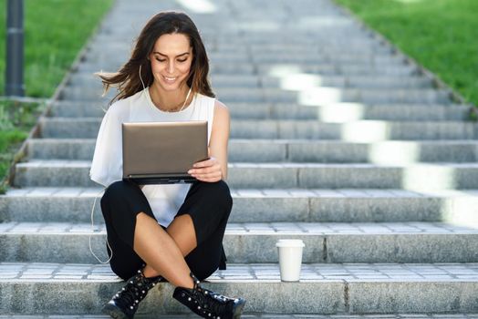 Young businesswoman having a videoconference with her laptop computer sitting on urban steps outdoors.