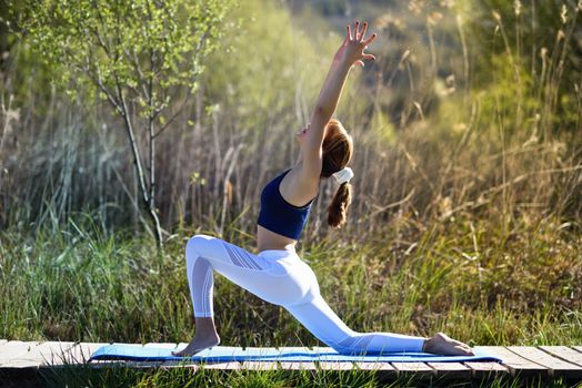 Young woman doing yoga in nature. Female wearing sport clothes on a wooden road.