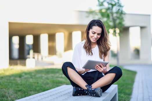 Middle-age woman using digital tablet sitting outdoors in urban background.