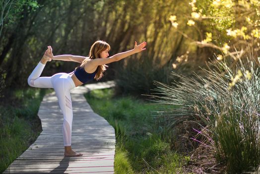 Young woman doing yoga in nature. Female wearing sport clothes.