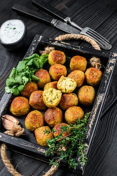 Roasted chickpeas falafel balls with garlic yogurt sauce in a wooden tray. Black wooden background. Top view.