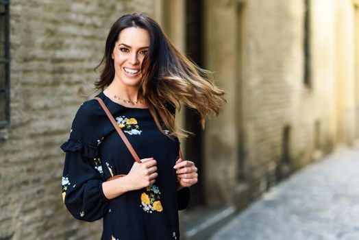 Young woman moving her long hair in urban background. Female in casual clothes with care hairstyle in Granada, Andalusia, Spain.