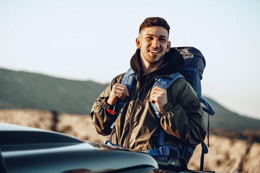 Portrait of a young traveler man in hiking equipment standing near his off-road car at dawn