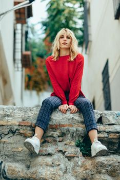Attractive young blond woman sitting on urban background. Blonde girl with red shirt enjoying life outdoors.