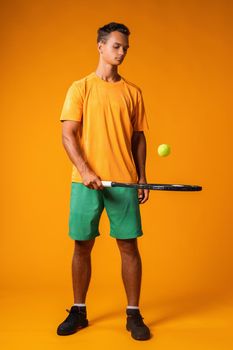 Full-length portrait of a tennis player man in action against orange background close up