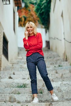 Happy young blond woman laughing on beautiful steps in the street. Smiling blonde girl with red shirt standing outdoors.