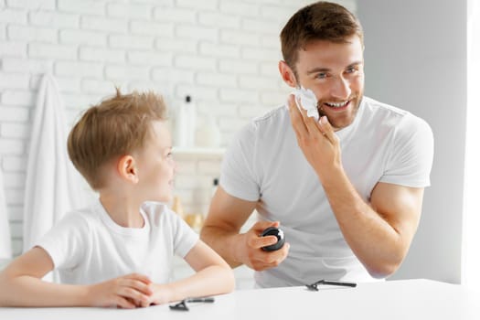 Father teaches his little son how to shave face in bathroom