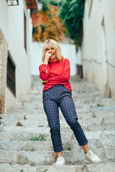 Happy young blond woman laughing on beautiful steps in the street. Smiling blonde girl with red shirt standing outdoors.