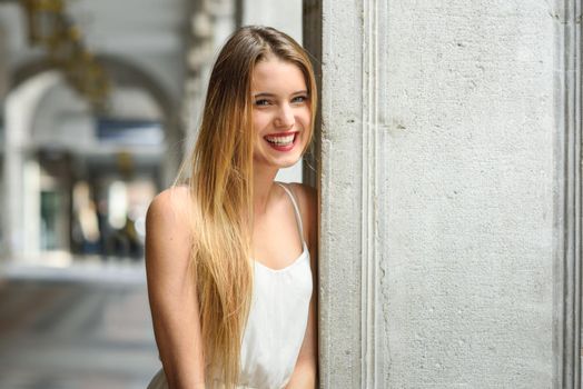 Portrait of beautiful blonde girl in urban background wearing white dress in urban background