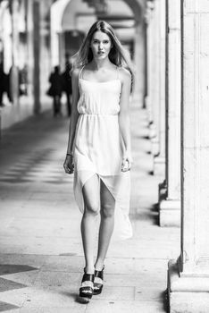 Portrait of beautiful blonde girl in urban background wearing white dress