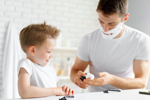 Father teaches his little son how to shave face in bathroom