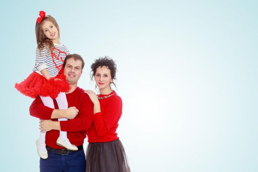 Happy young family dad mom and a little girl in bright red outfits . Dad holds daughter on hands.On the pale blue background.