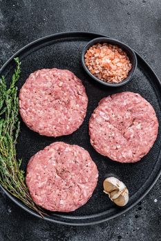 Raw chicken turkey patty, minced meat cutlets on a plate with thyme. Black background. Top view.