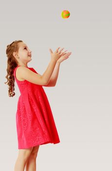 Cute little girl in a bright orange dress, throws a little ball.On a gray background.