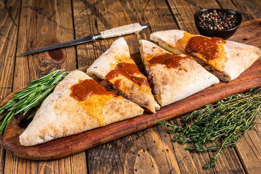 Cut and sliced Calzone closed pizza with ham and cheese on wooden board with hot tomato sauce. wooden background. Top view.