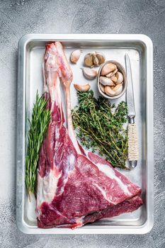 Uncooked Raw goat or lamb leg with herbs in baking tray. White background. Top view.