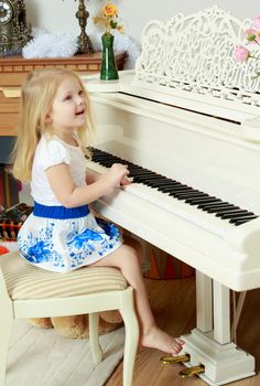 A little blonde is playing on a white grand piano.