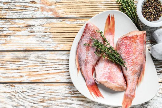 Whole raw red snapper fish on a plate. White wooden background. Top view. Copy space.