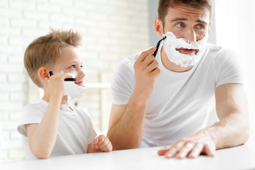 Father teaches his little son how to shave face in bathroom