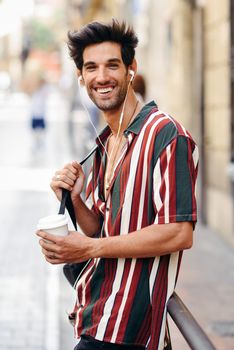 Young male traveler enjoying the streets of Granada, Spain. Man using earphones carrying backpack and a take-away glass.