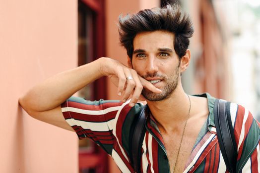 Attractive young man with dark hair and modern hairstyle wearing casual clothes in urban background.