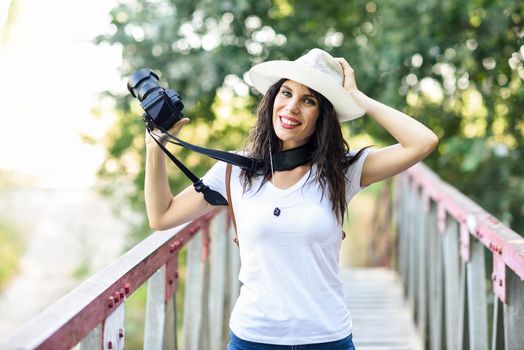 Beautiful hiker young woman taking photographs with a mirrorless camera, wearing straw hat, hiking in the countryside.